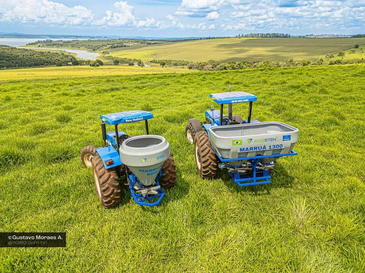Vista aérea dos dois tratores com os distribuidores Marruá no pasto, com campo e lago ao fundo