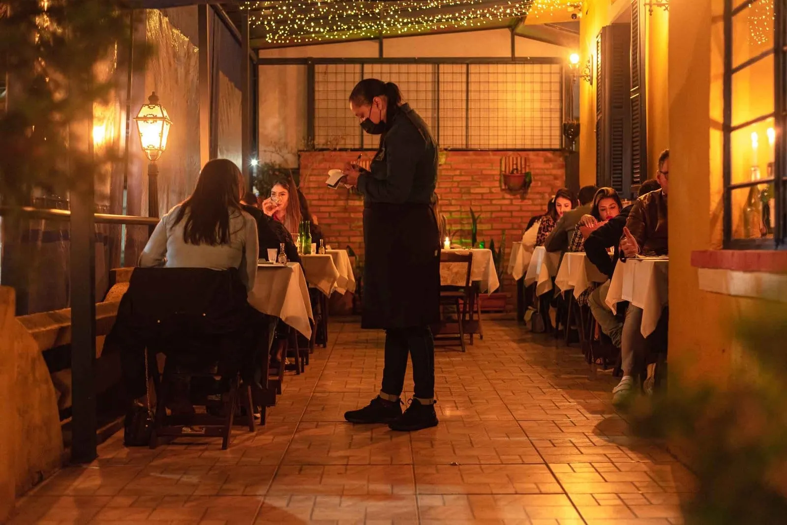 Salão do Alicita Bistrô à meia-luz, com garçom e clientes à mesa