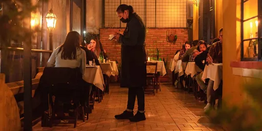 Salão do Alicita Bistrô à noite, com clientes nas mesas, luz de velas e um garçom de pé no corredor