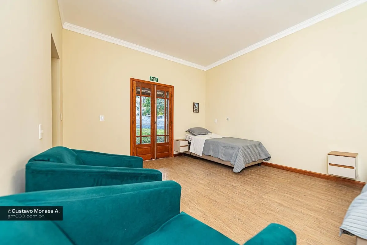Suíte com poltronas verdes, cama de solteiro e porta de madeira com vidro para a área externa