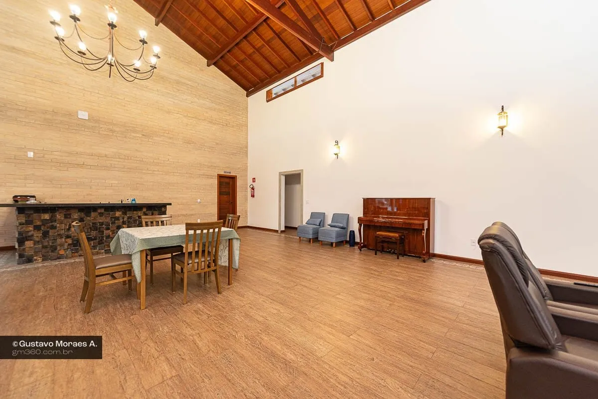 Salão com pé-direito alto, forro de madeira, lustre, mesa de jantar e piano ao fundo