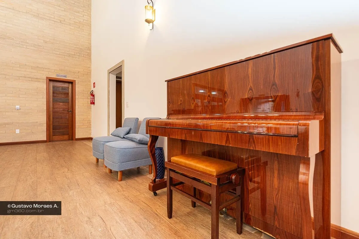 Piano de madeira e banqueta em sala com poltronas ao fundo