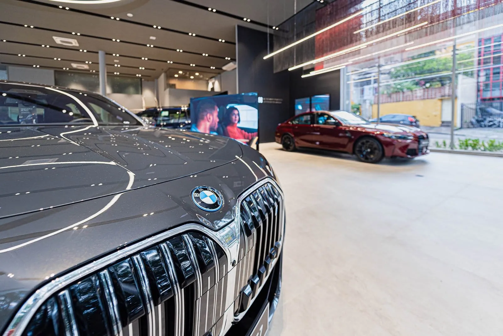 Grade dianteira de um BMW cinza em primeiro plano, com o salão de exposição ao fundo