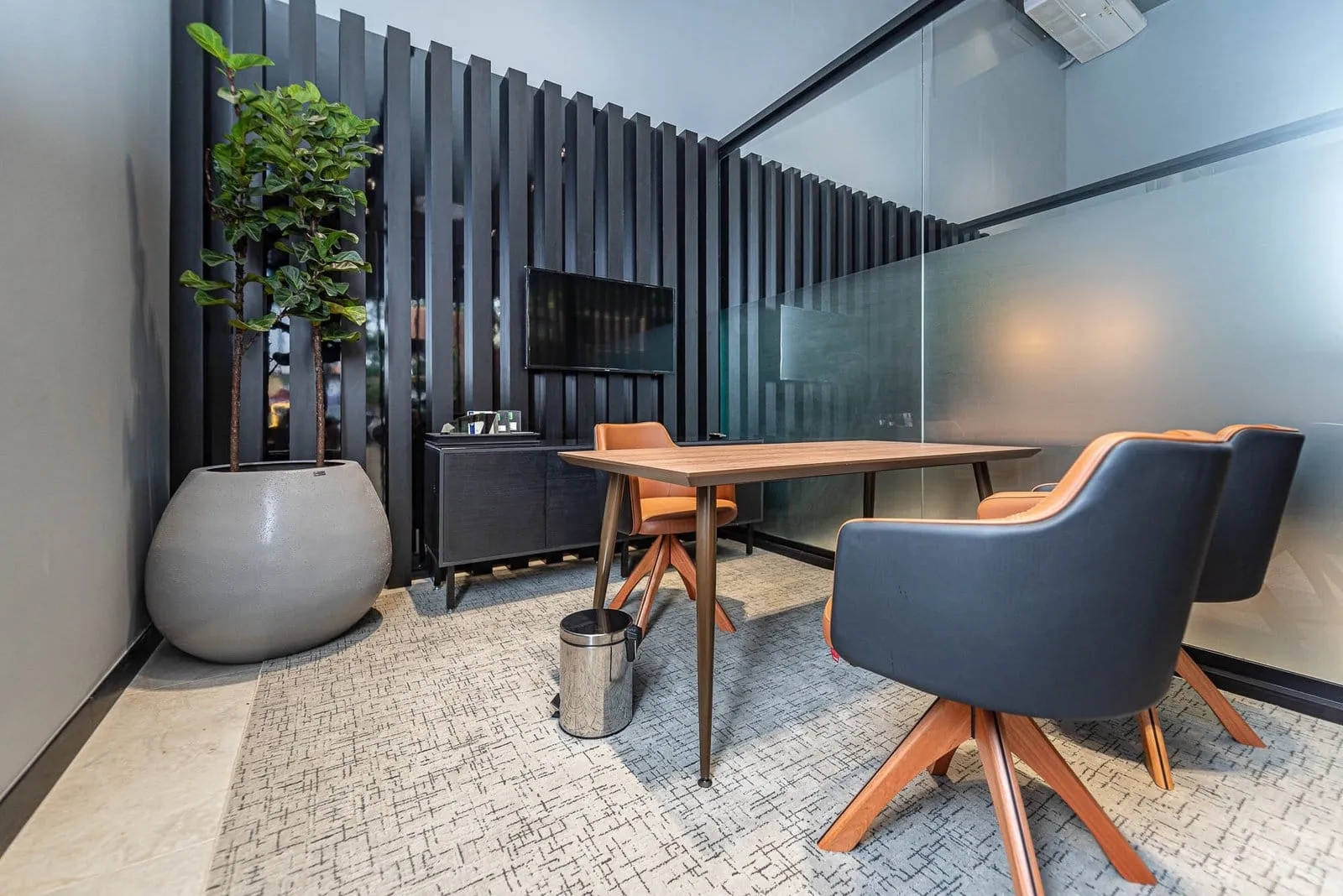 Sala de atendimento com mesa de madeira, poltronas escuras e parede ripada