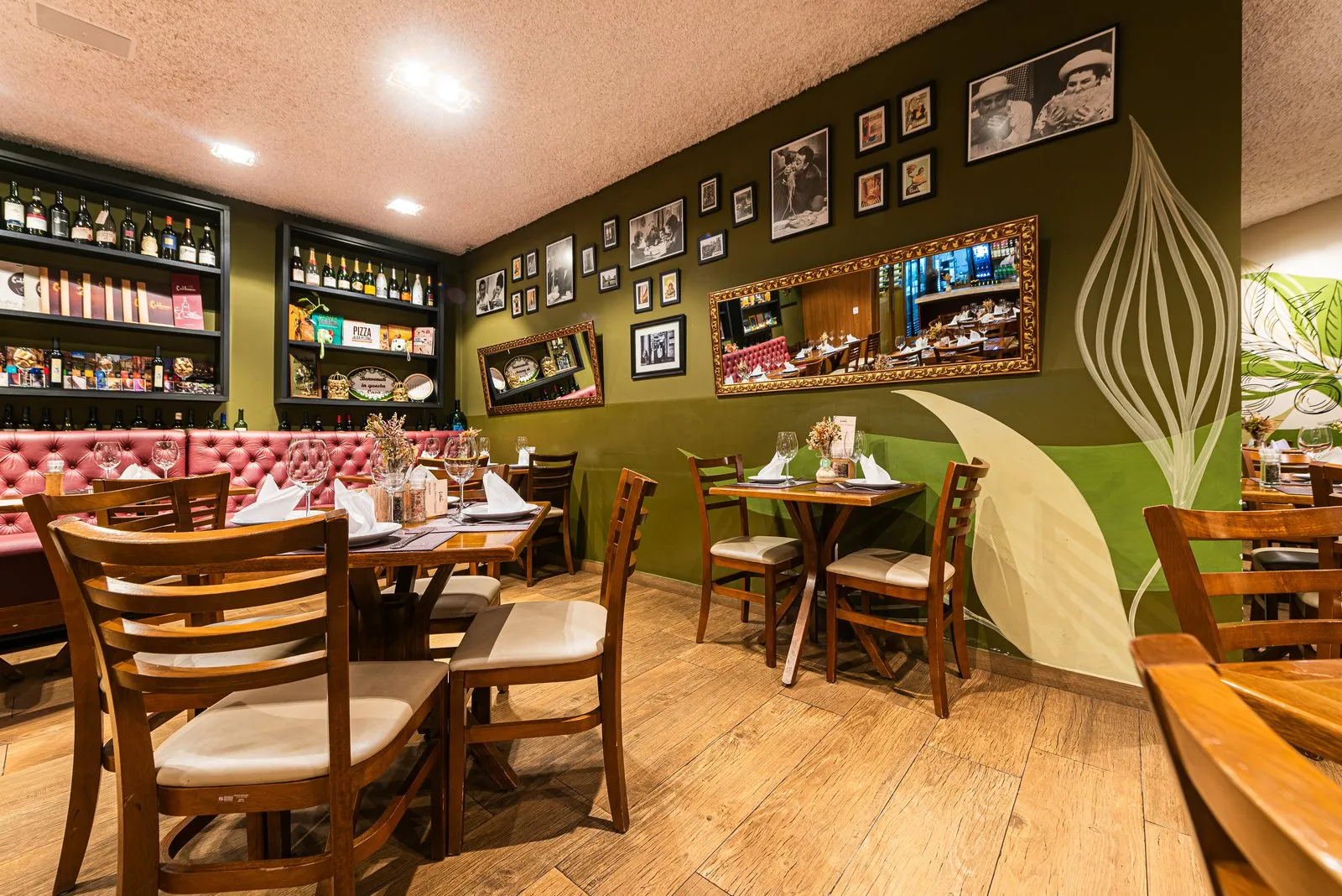 Parede verde-oliva da Cantina Castellammare com fotos em preto e branco, espelhos dourados, banco capitonê rosé e estantes de vinhos