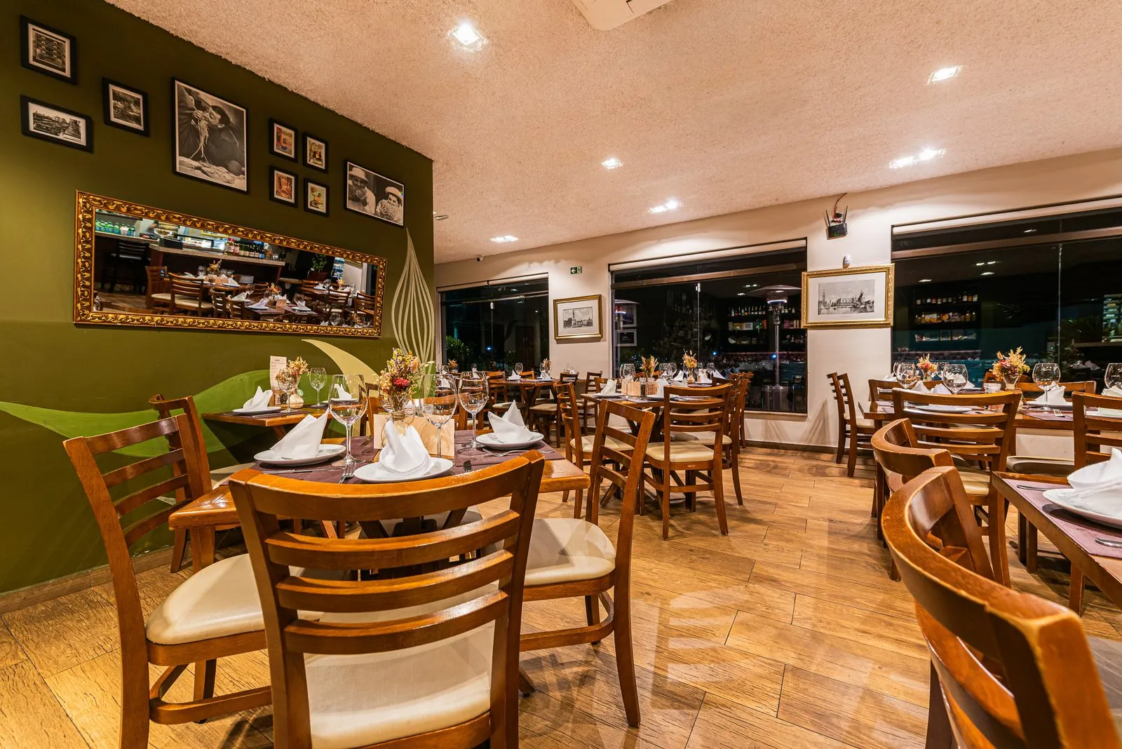 Salão da Cantina Castellammare com parede verde, fotos em preto e branco e espelho dourado de um lado e janelas com gravuras emolduradas do outro