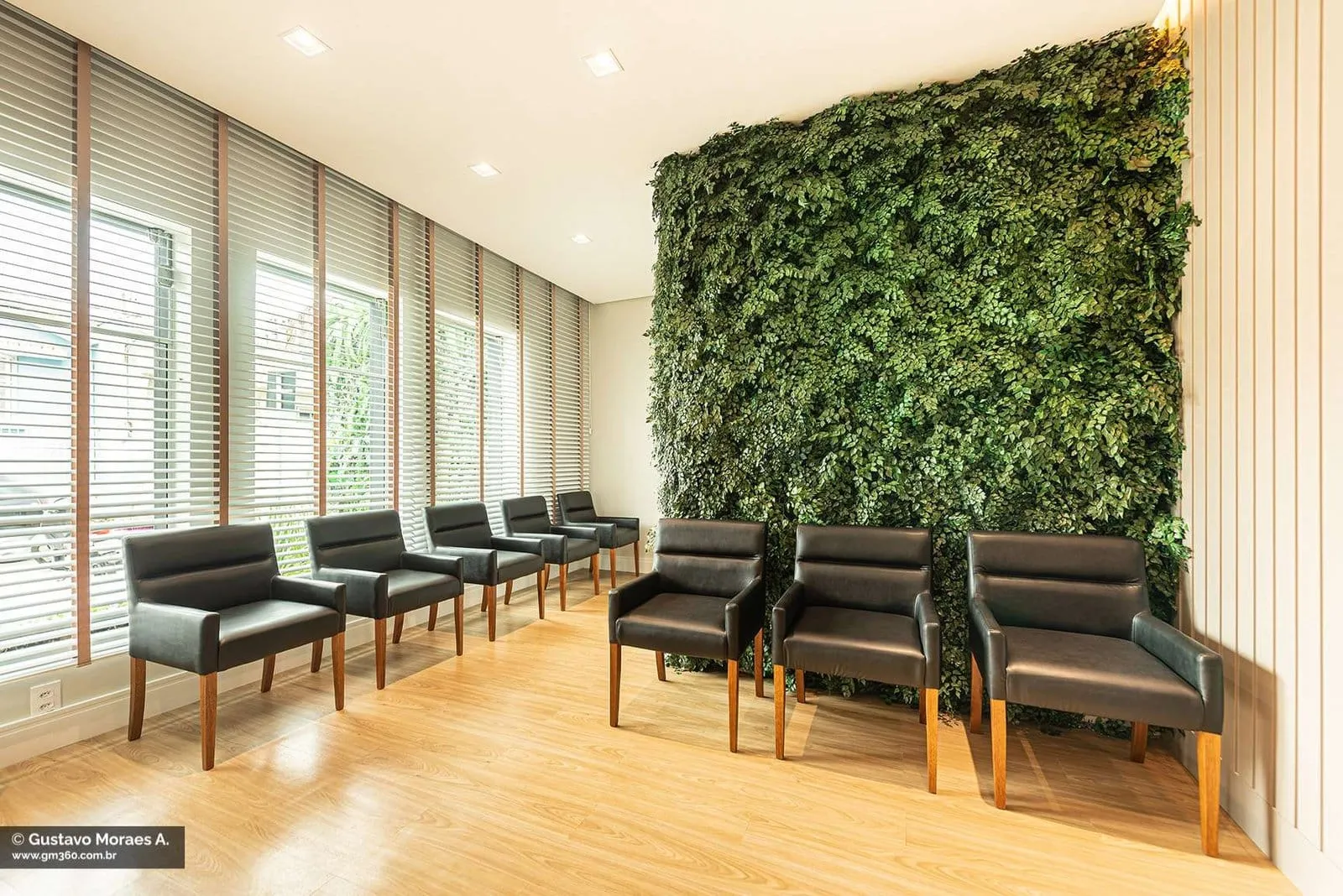 Sala de espera da Art Dentaire com parede verde de plantas e poltronas pretas, em Itapetininga