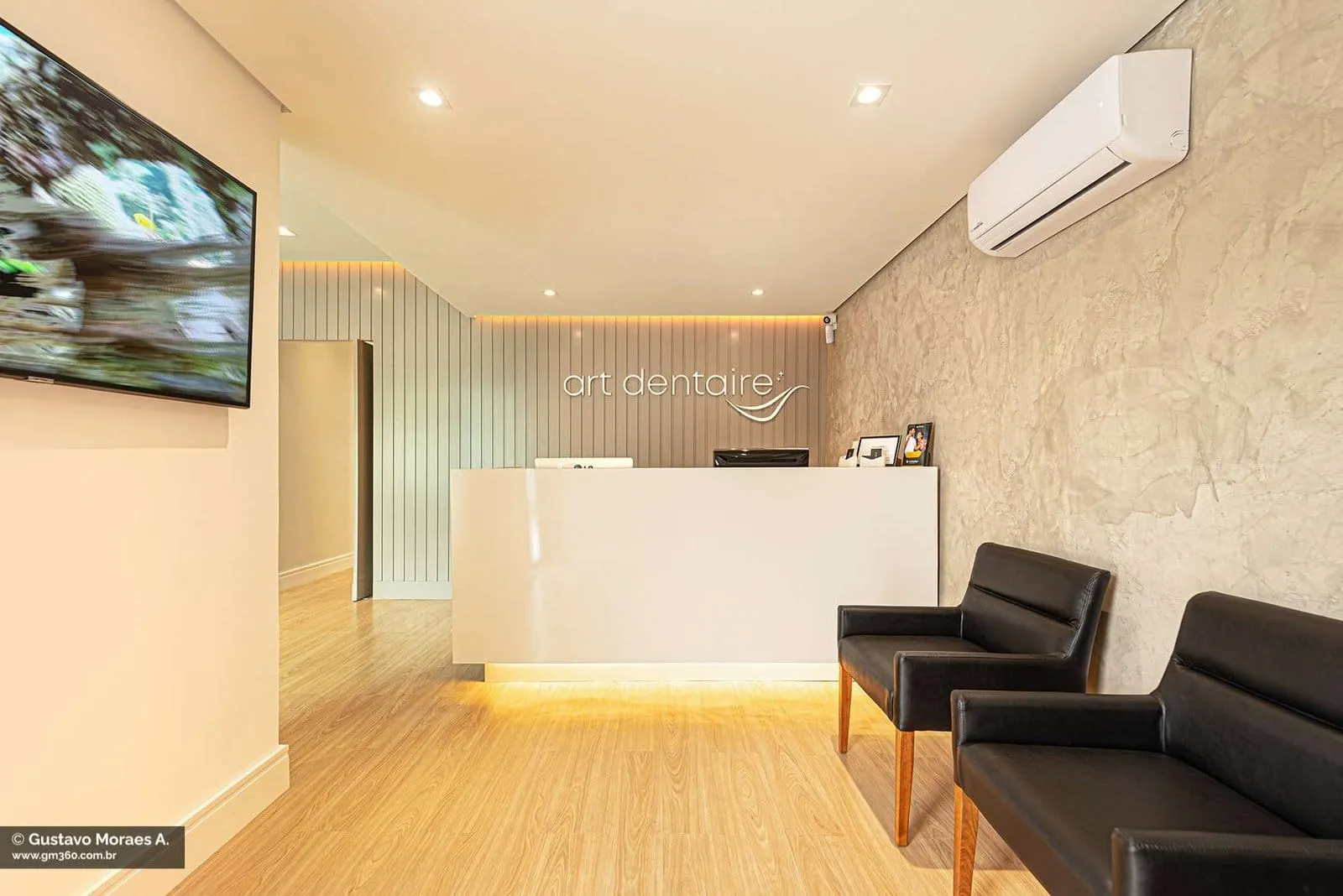 Recepção da Art Dentaire com balcão branco iluminado, poltronas pretas e piso de madeira