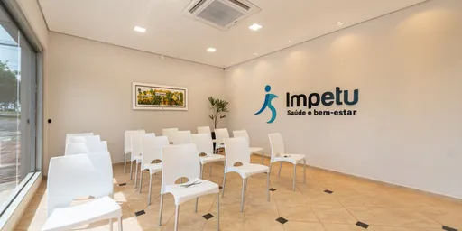 Sala ampla da Clínica Impetu com cadeiras brancas enfileiradas e o logotipo da clínica na parede