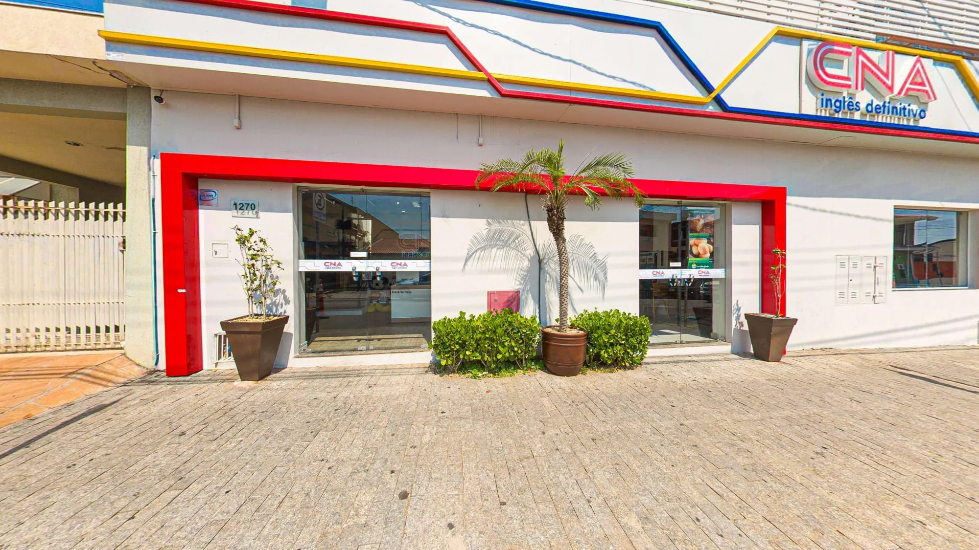 Fachada do CNA Itapetininga, branca com moldura vermelha na entrada de vidro, faixas coloridas e o letreiro CNA inglês definitivo