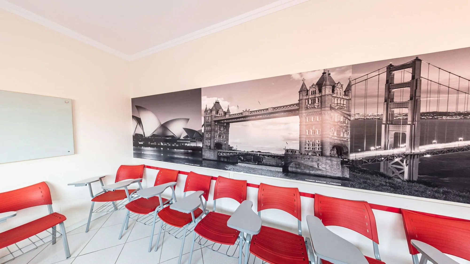 Sala Australia do CNA Itapetininga, com cadeiras vermelhas e painel em preto e branco da Ópera de Sydney, da Tower Bridge e da Golden Gate