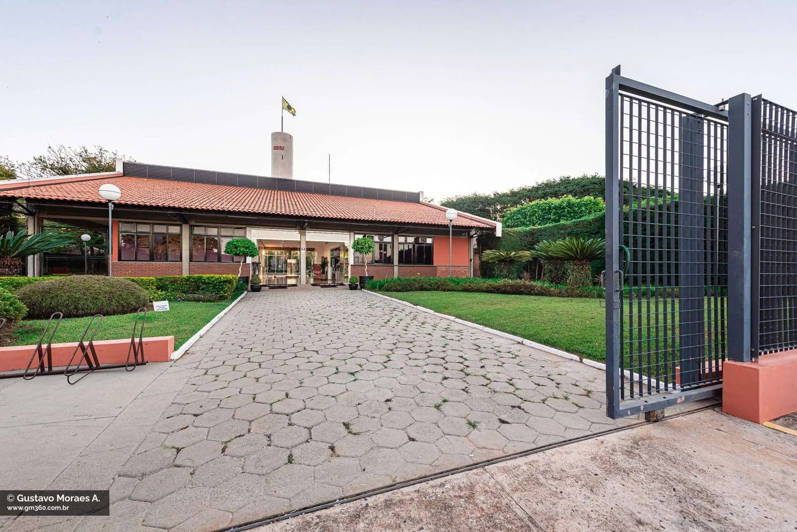 Caminho de entrada do SESI Itapetininga, com jardim e portão