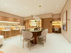Sala de jantar do apartamento decorado do Grand'Oro Vila Barth, com mesa oval de mármore verde, lustre de bolhas de vidro, cristaleira iluminada e a bancada da cozinha ao fundo