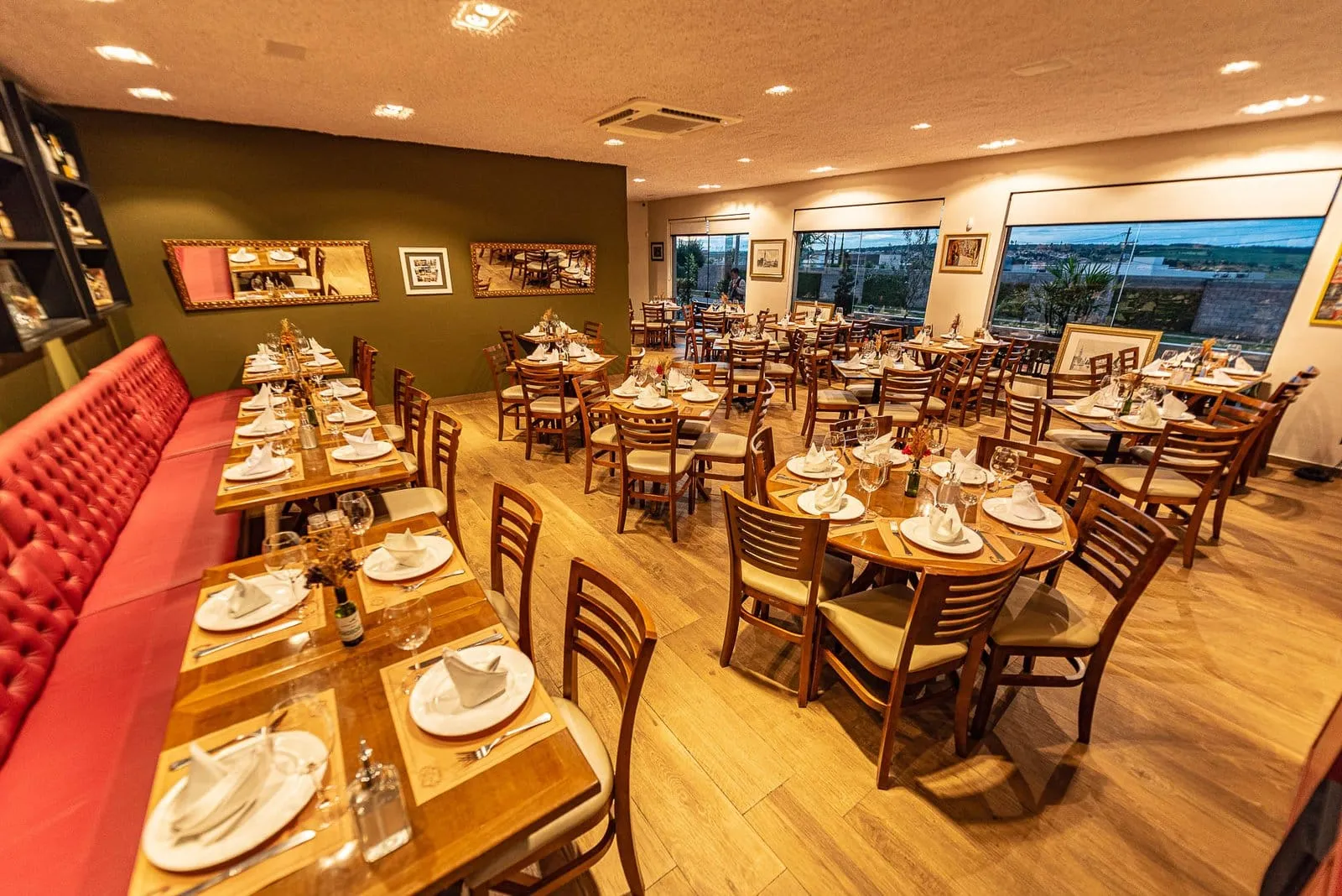 Salão da Cantina Castellammare com sofá capitonê vermelho e mesas postas, em Itapetininga
