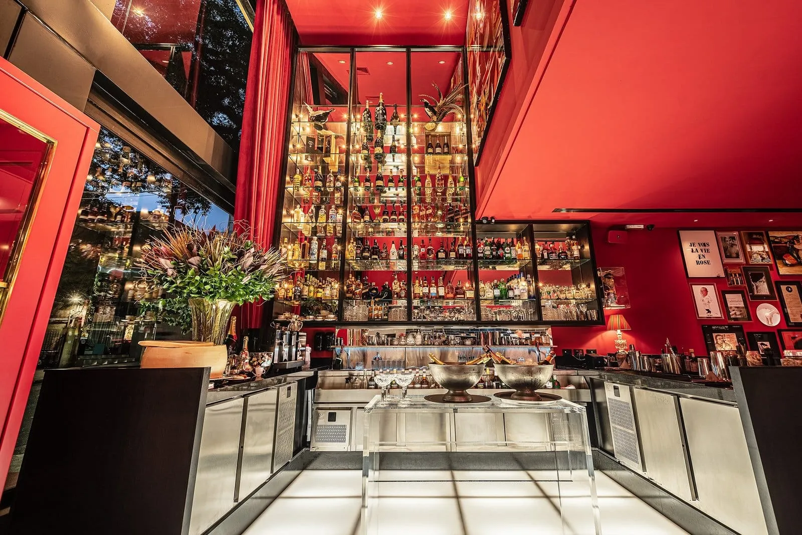 Bar do Les Présidents com cristaleira de garrafas em pé-direito duplo e balcão de inox