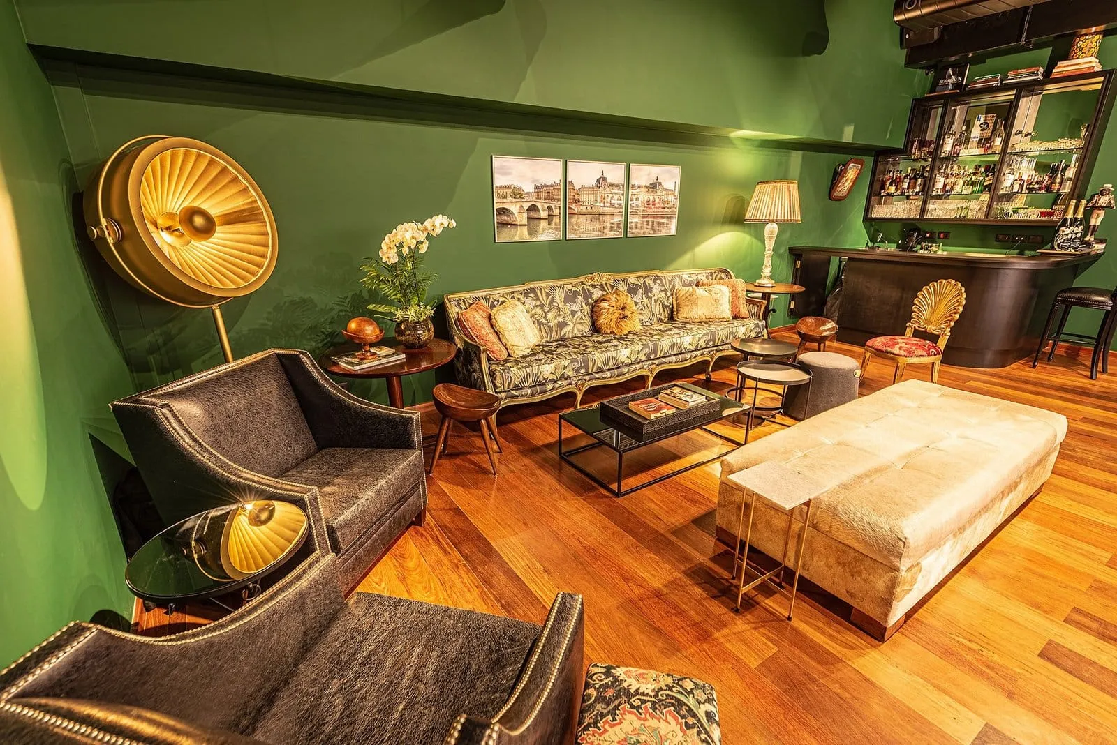 Poltronas de couro, luminária dourada e sofá estampado no Clube dos Ministros, de paredes verdes
