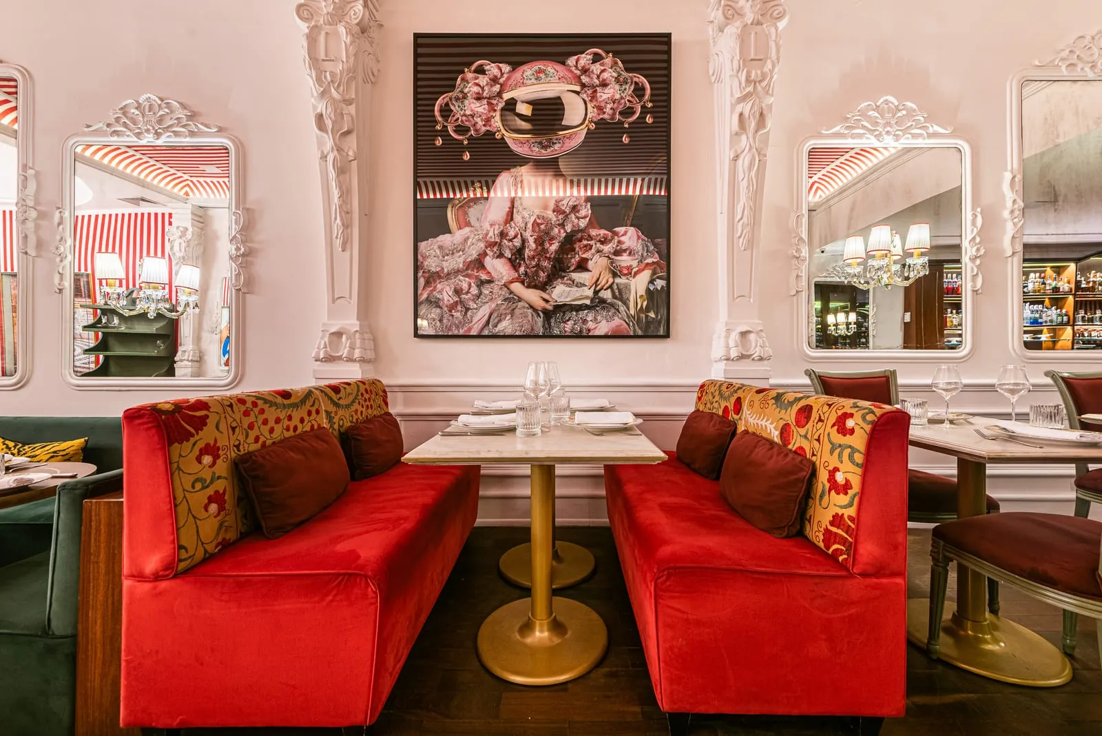 Dois sofás de veludo vermelho frente a frente com encosto bordado, mesa de mármore e quadro contemporâneo entre colunas brancas entalhadas