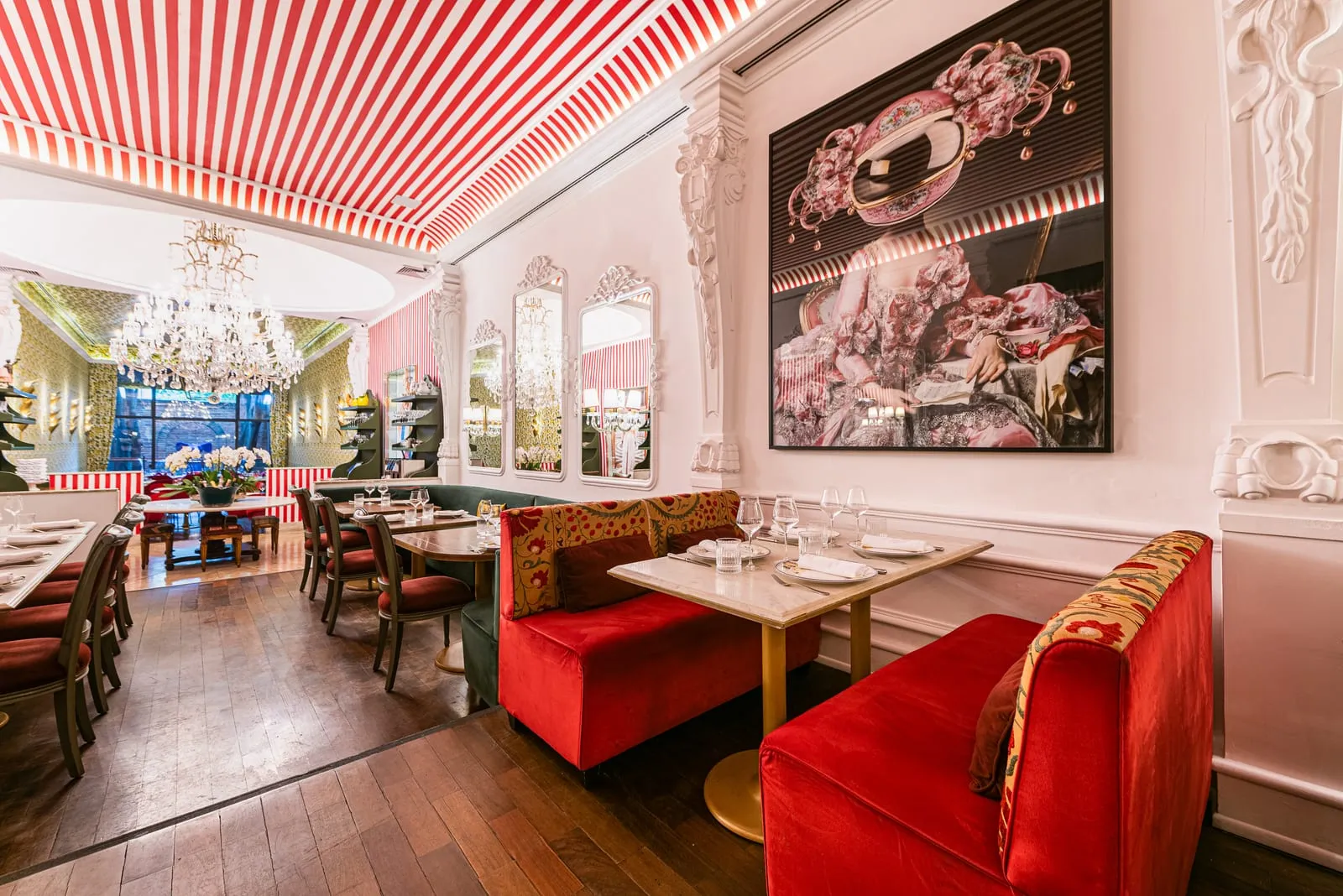 Sofás de veludo vermelho e mesa posta sob um quadro grande, com vista para o lustre de cristal e a sala de papel de parede de limões