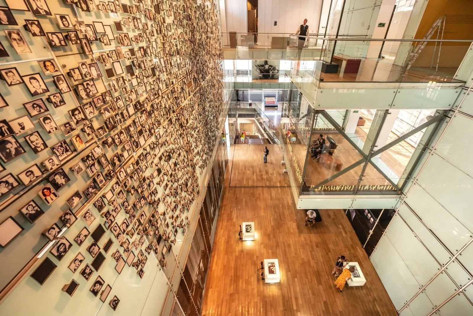 Parede coberta de retratos e passarelas de vidro em museu, vista do alto