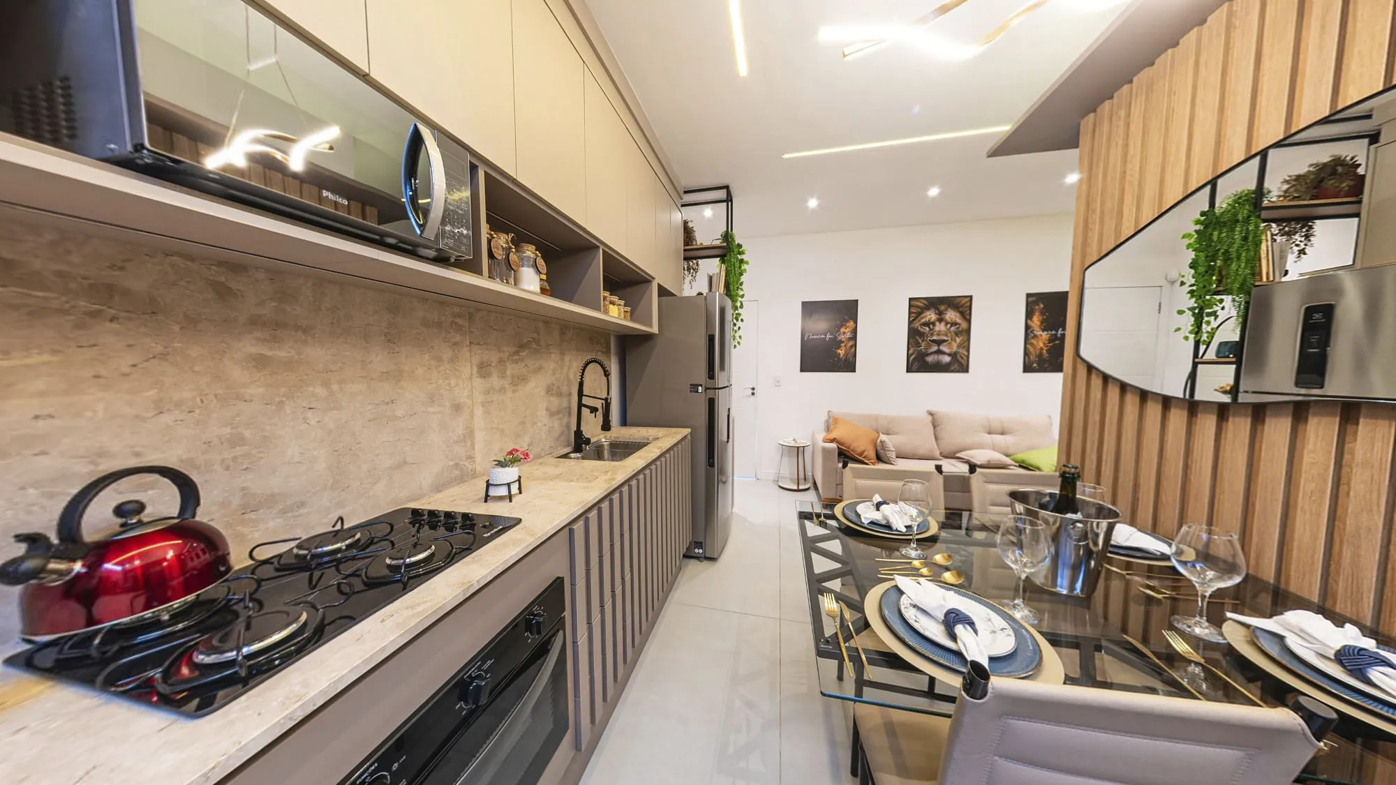 Cozinha linear com armários claros, cooktop, bancada de pedra e frente ripada, ao lado da mesa de jantar posta