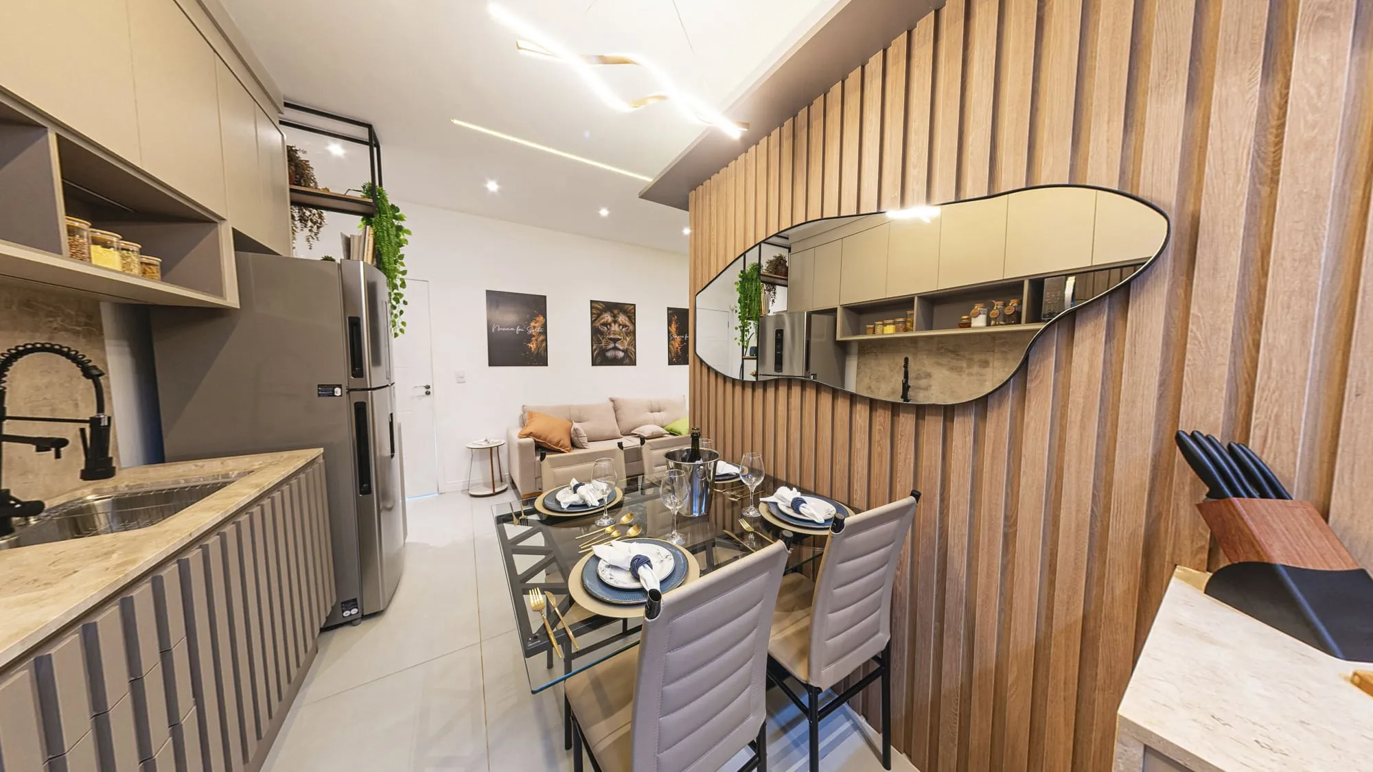 Mesa de jantar de vidro posta para quatro, junto ao painel ripado com espelho orgânico, com a cozinha à esquerda e a sala ao fundo