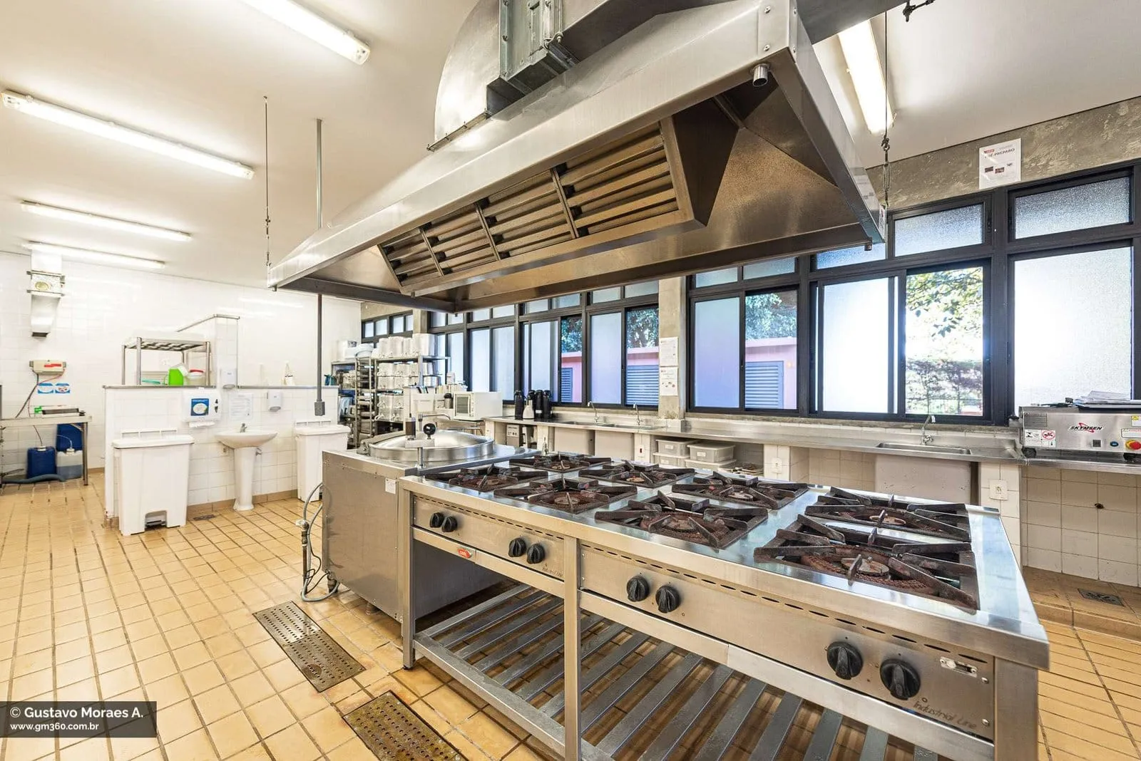 Cozinha industrial com fogões, coifa e bancadas de inox