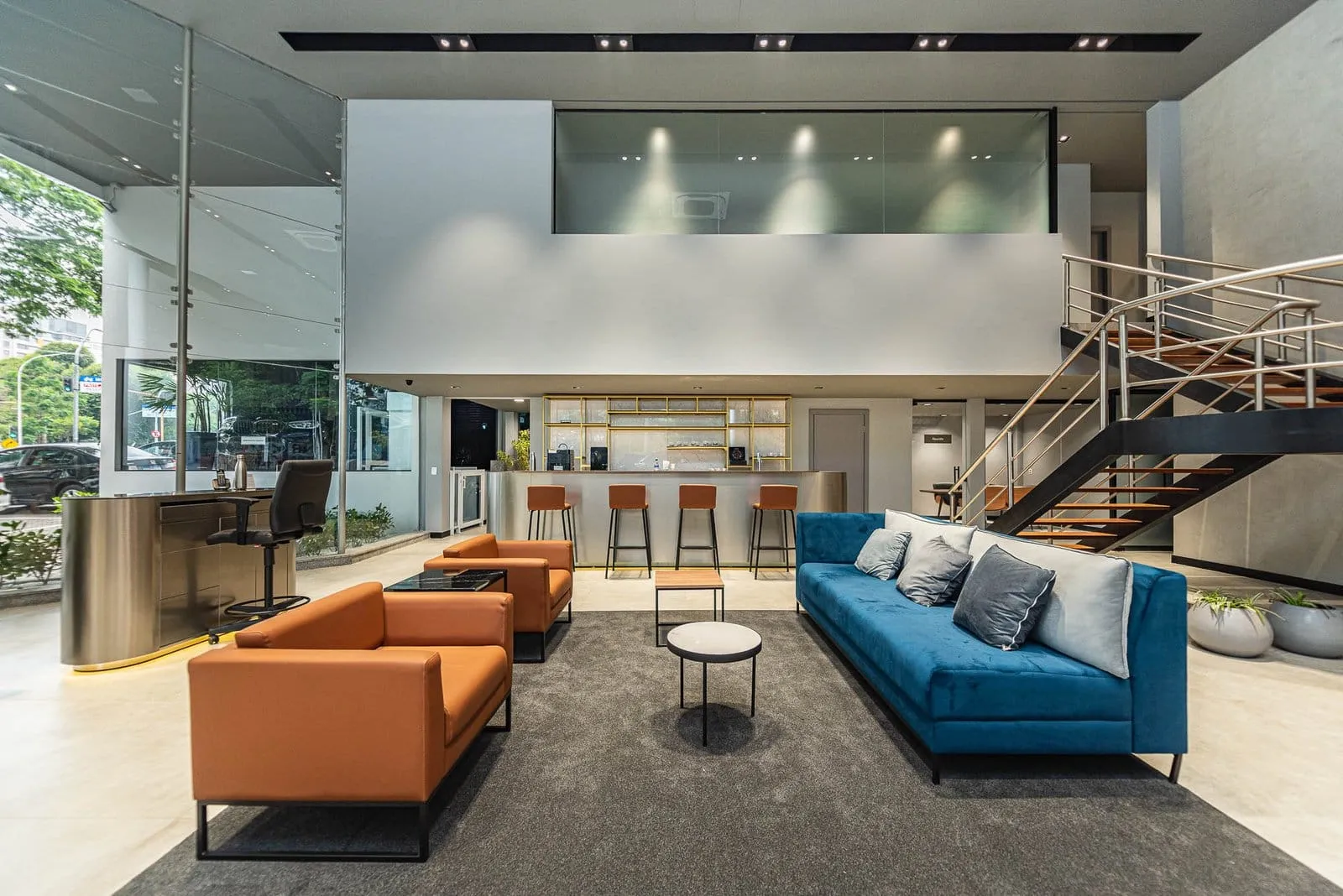 Lounge com sofás laranja e azul e escada para o mezanino da BMW Osten Perdizes
