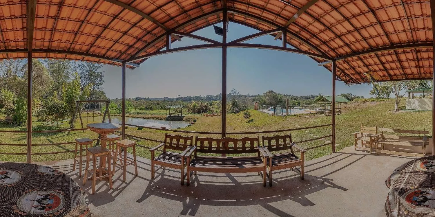 Varanda coberta do Sítio Santa Maria, em São Miguel Arcanjo, com mesas de madeira e vista para o campo