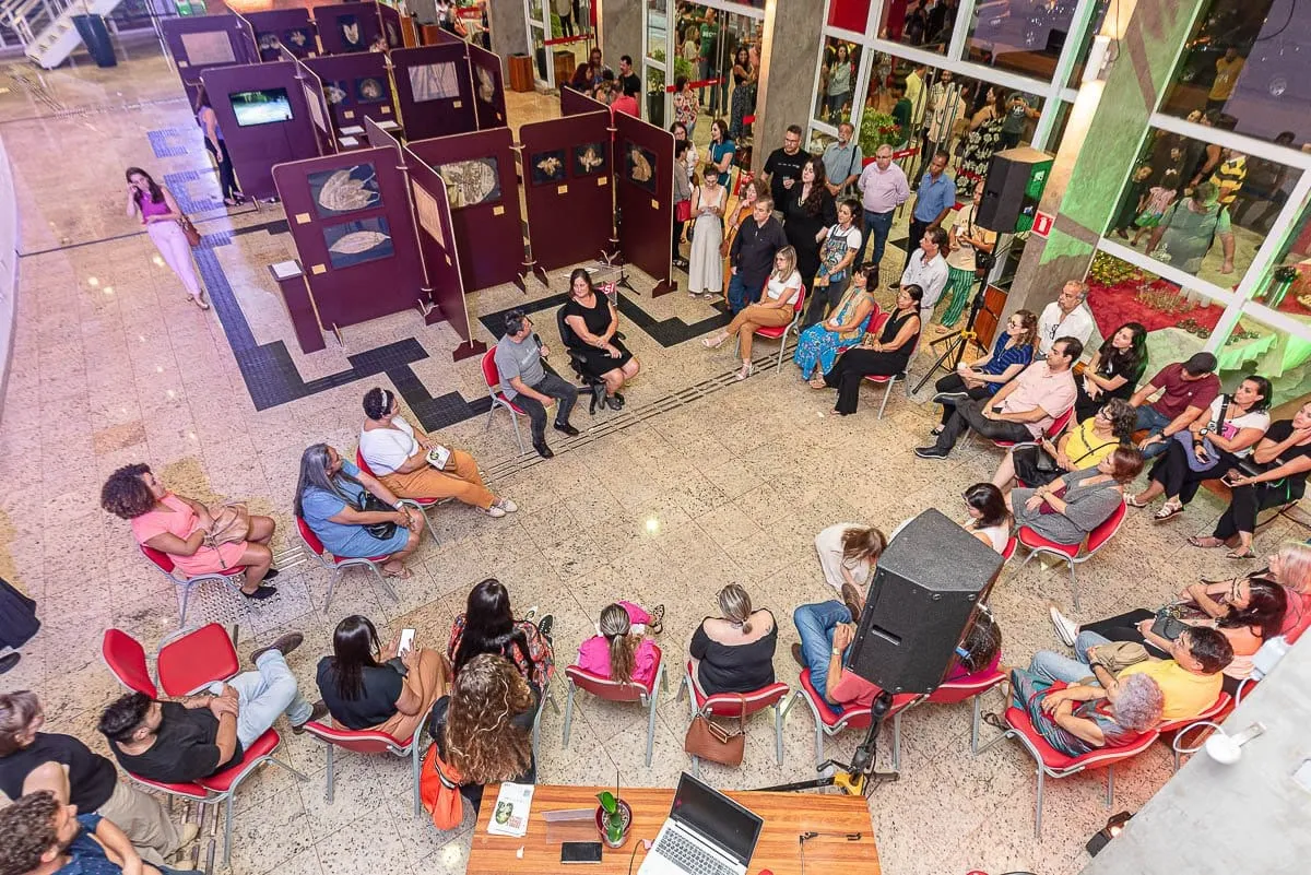 Vista do alto da conversa de abertura, com o público sentado em roda no saguão ao lado da exposição